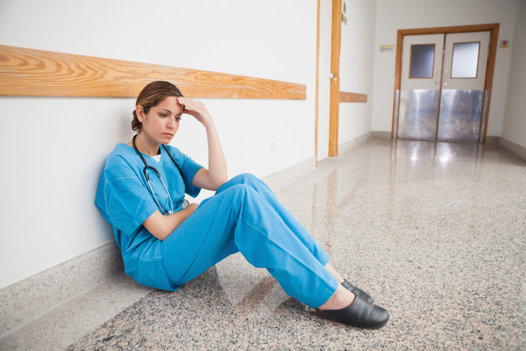 Nurse sitting on the floor hand on forehead thinking