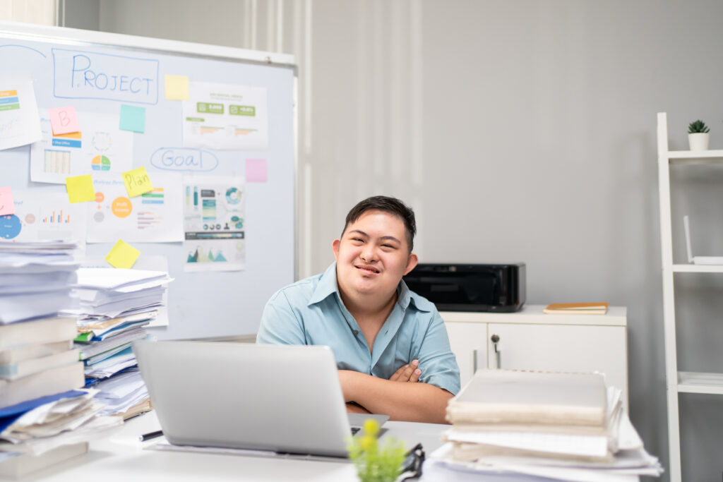 Portrait of Asian young businessman with down syndrome work in office. Employee man worker people sitting on table, planning project alone in corporate workplace then smiling, looking at camera.