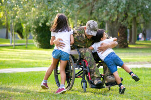 Happy disabled military man in wheelchair returning home and hugging kids. Veteran of war or family reunion concept