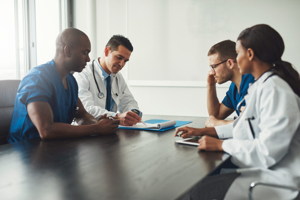 Multiracial medical team having a meeting with doctors in white lab coats and surgical scrubs seated at a table discussing a patients records