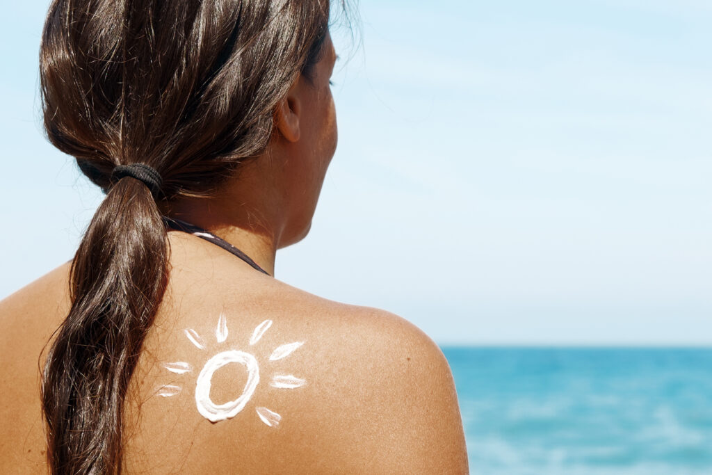 Sun drawn with sunscreen on the shoulder of a female with tanned skin. Skin cancer prevention, skin protection concept. Sea background.
